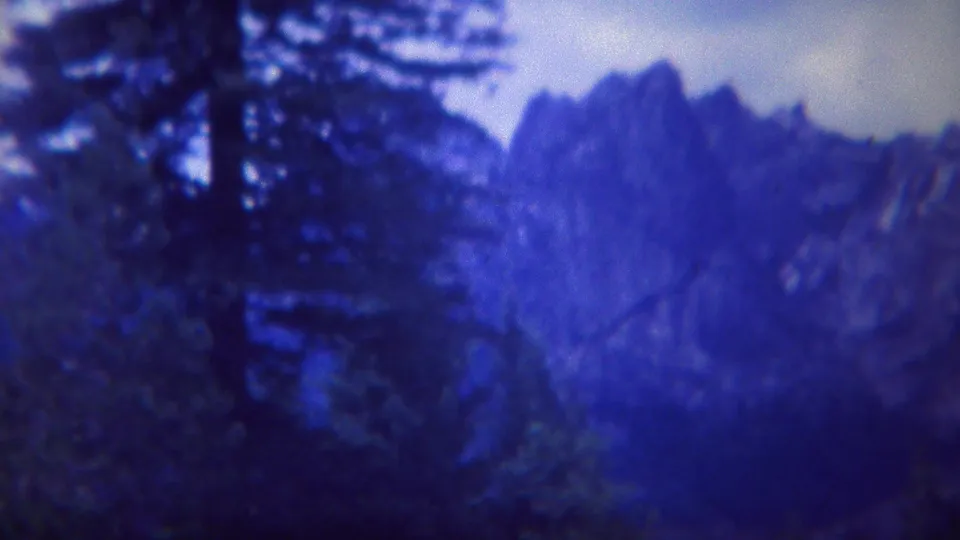 1967 Yellowstone 8mm frame showing a dark evergreen at left with rugged blue-toned peaks extending across the background.
