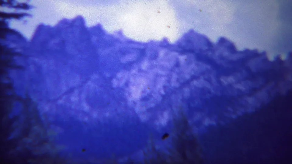 1967 Yellowstone 8mm frame showing a soft blue mountain ridge under a pale sky with evergreen edges.