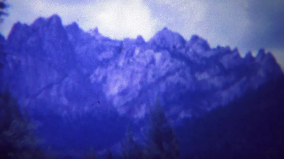 1967 Yellowstone 8mm frame of jagged blue mountain peaks above a dark wooded foreground.