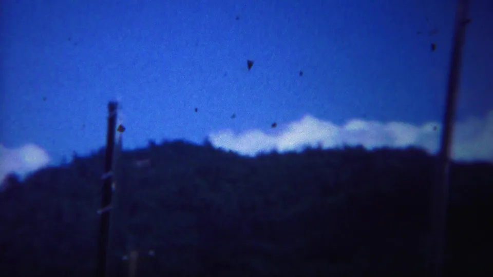 1967 Yellowstone frame showing a dark forested hill, blue sky, clouds, and utility poles entering the scenic view.