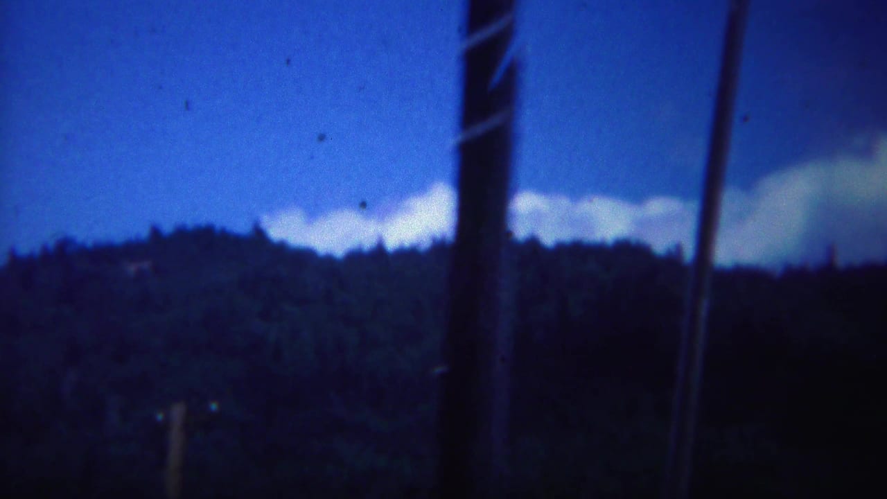 Dark wooded ridgeline beneath a deep blue sky with blurred foreground poles or trunks.