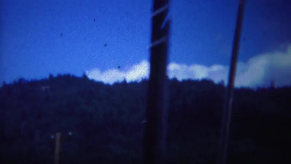 1967 Yellowstone-area 8mm frame showing a dark forested ridge under blue evening light with blurred foreground verticals.