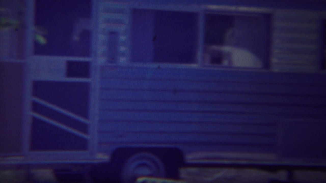 Blue travel trailer with an open door and windows at a campsite.