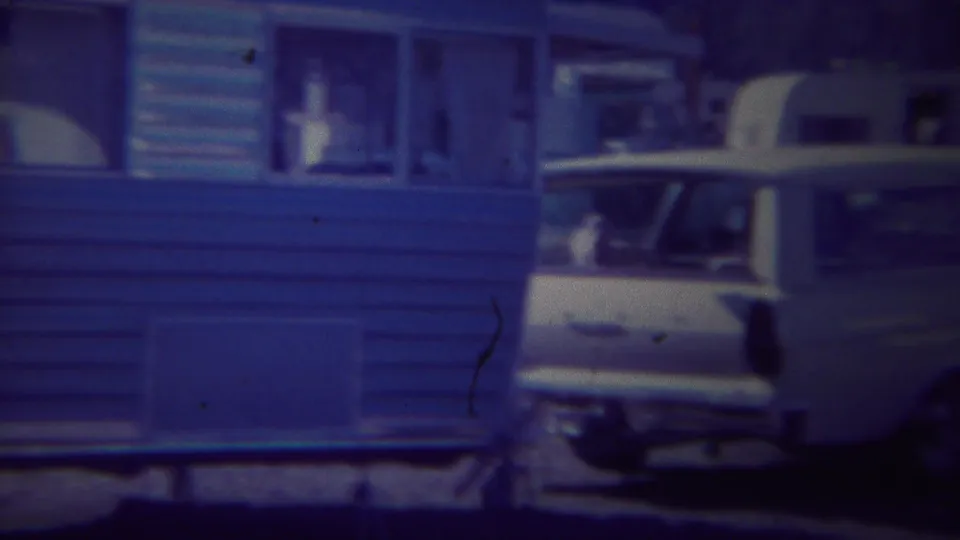 A white station wagon is parked close to the blue travel trailer, suggesting a 1967 Yellowstone camping stop.