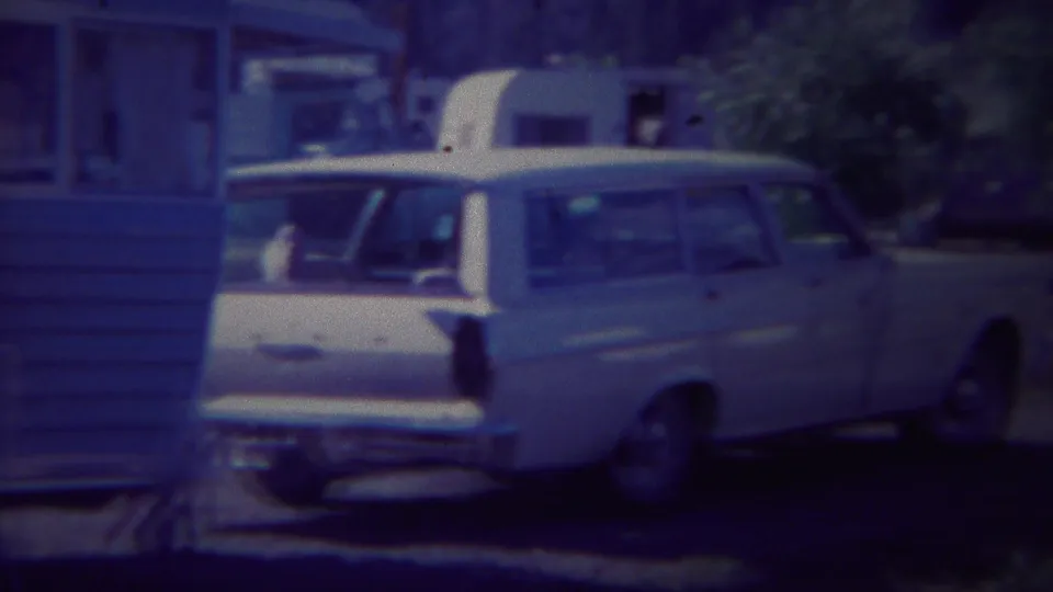 White station wagon and blue travel trailer are framed together at a wooded Yellowstone campsite in 1967 home-movie footage.