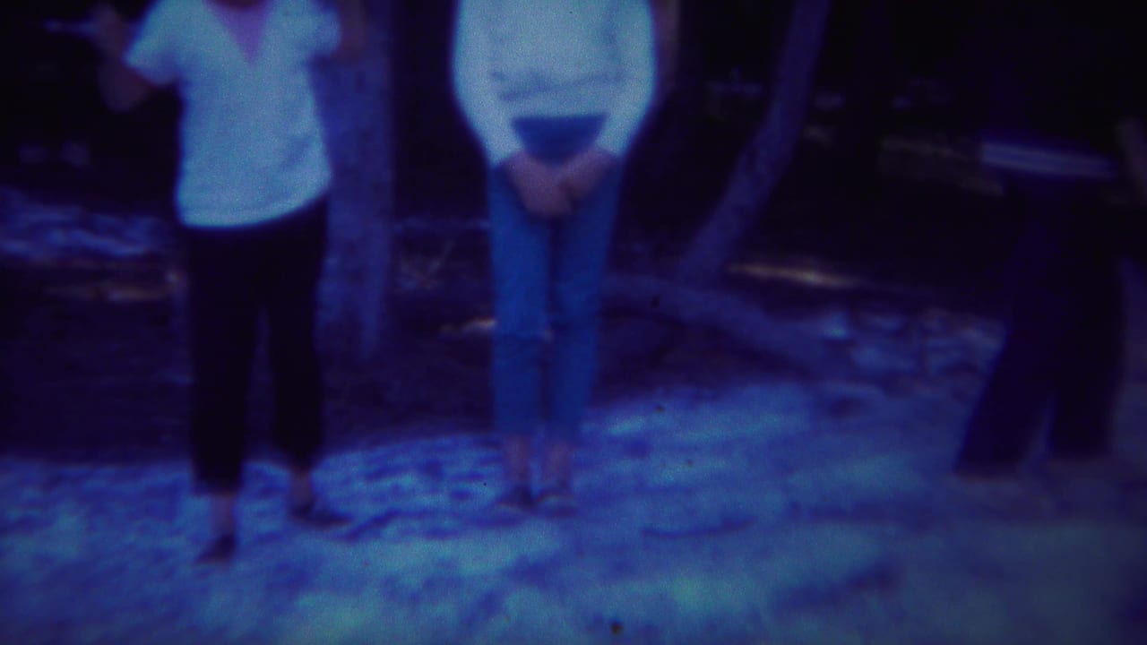 Two people stand near a tree while a third figure is partly visible at the edge.