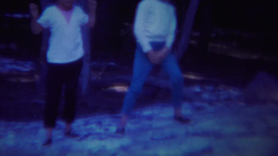 Two visible visitors stand on uneven ground in the Yellowstone woods, captured in grainy 1967 home-movie footage.