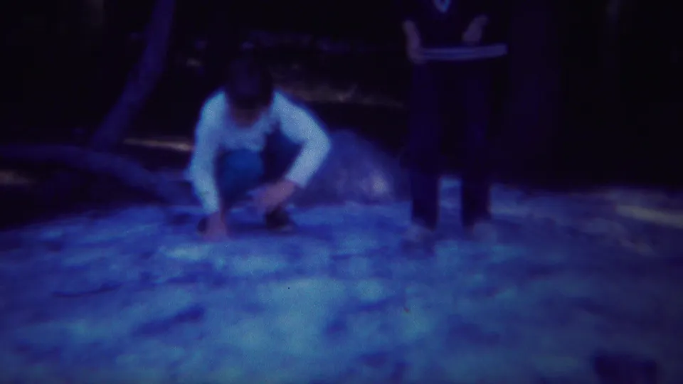 A person crouches on the wooded ground as another stands nearby, in blue-cast Yellowstone 8mm home-movie footage.
