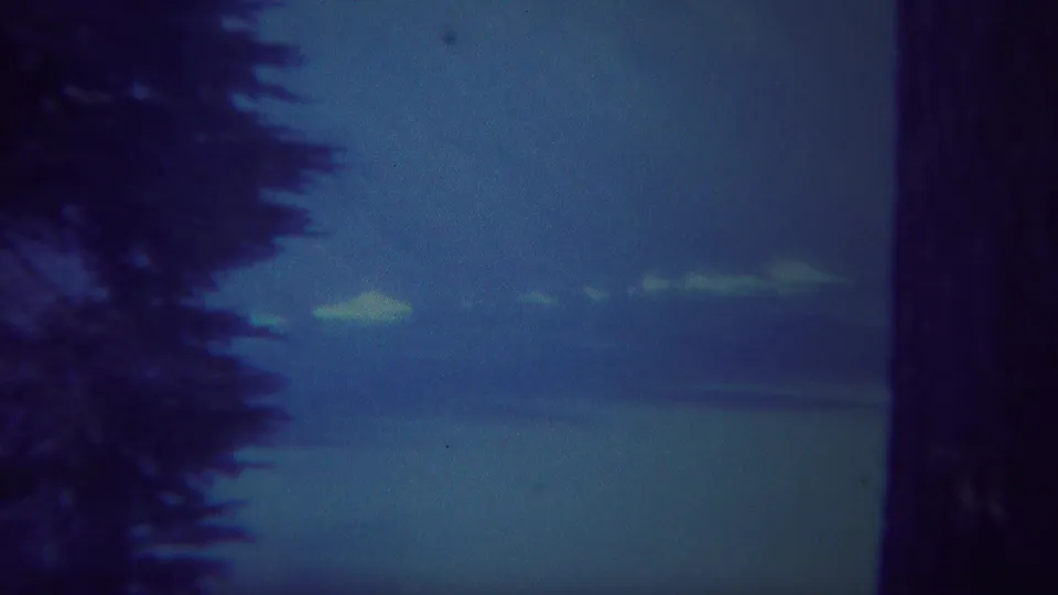1967 Yellowstone-area 8mm frame showing a dark tree trunk at the edge of a blue sky and low cloud horizon.