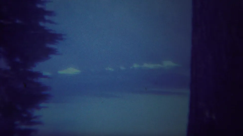 1967 Yellowstone home-movie view of a blue misty lake, distant mountains, and dark evergreen silhouettes.