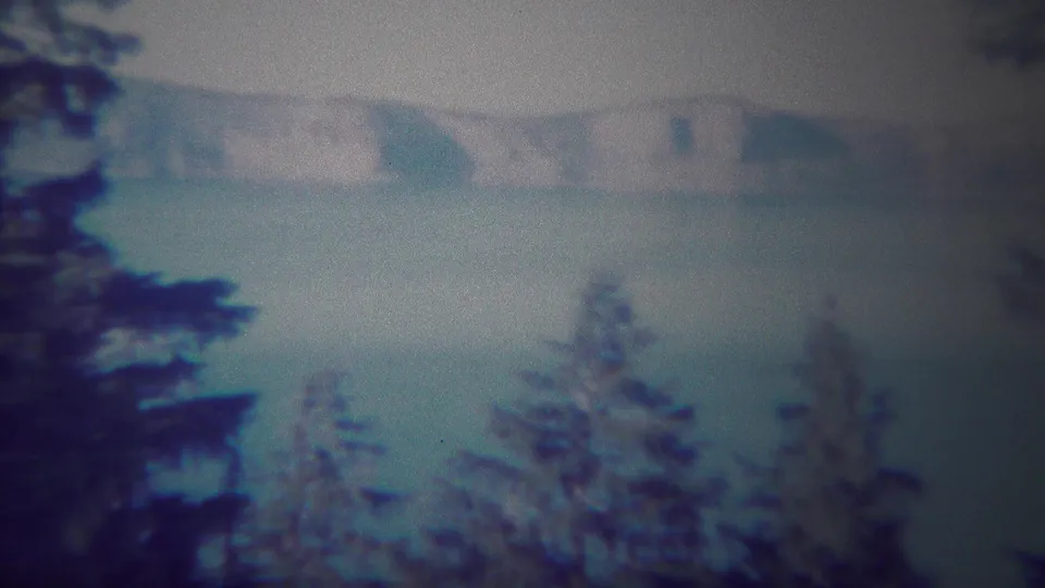 Yellowstone lake and fog-softened mountains appear beyond dark evergreen treetops in soft 8mm color footage.