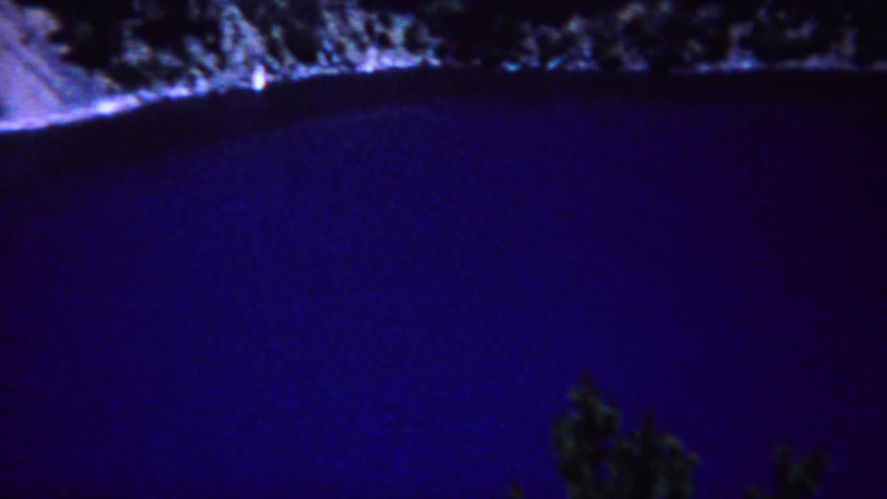Dark blue lake bordered by a rocky, tree-lined shore.