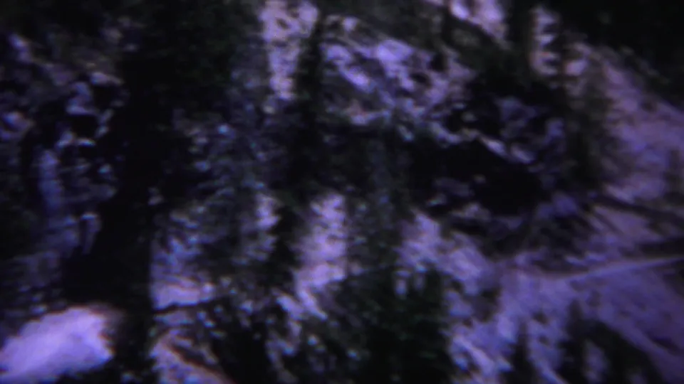 1967 Yellowstone mountain frame with conifers, patchy snow, and rugged terrain rendered in grainy 8mm twilight color.