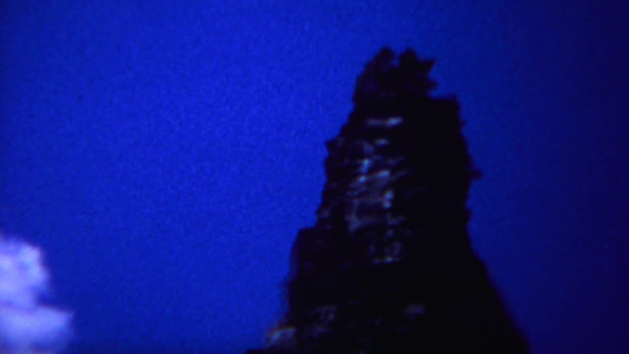 1967 Yellowstone home-movie frame showing a dark rocky peak rising into a blue night sky, with faint cloud at the left edge.