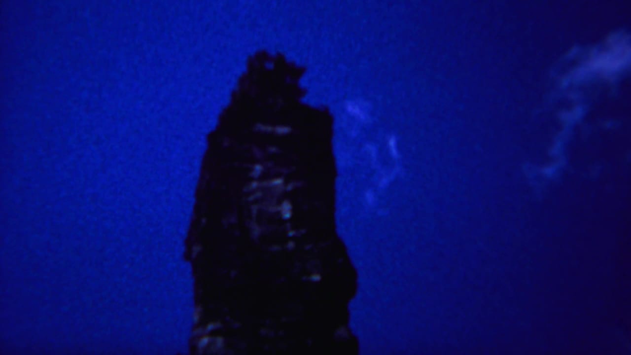 Tall dark rock formation centered against a blue sky with faint cloud texture on the right.