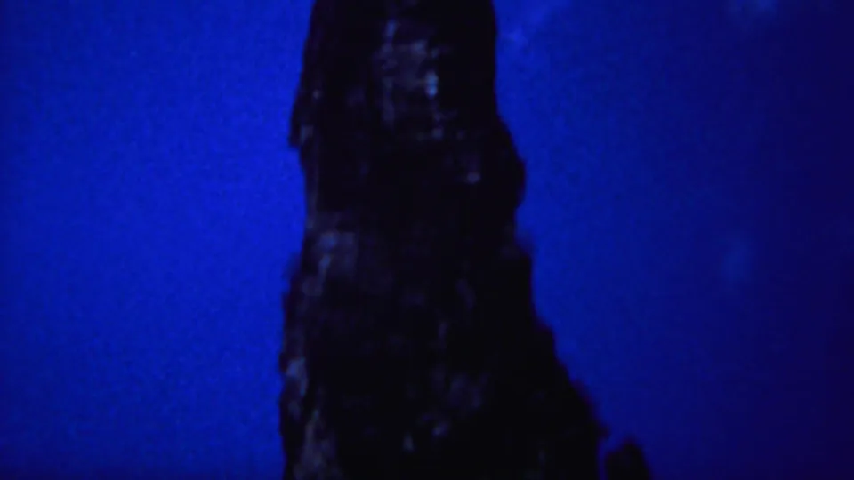 Blue-tinted 1967 Yellowstone frame showing a dark rock spire rising from the lower frame under an open night sky.