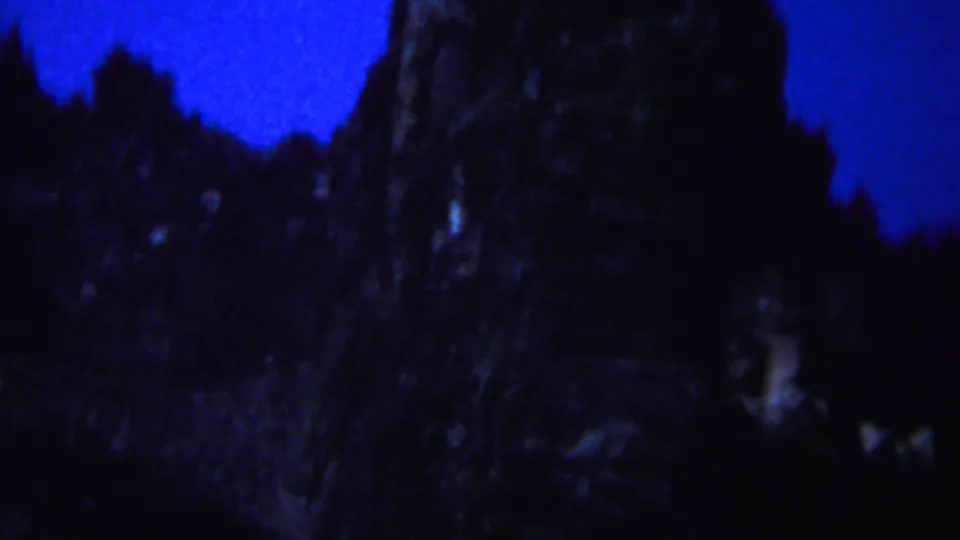 1967 Yellowstone frame showing a shadowed cliff face and smaller rocky peaks against a saturated blue sky.