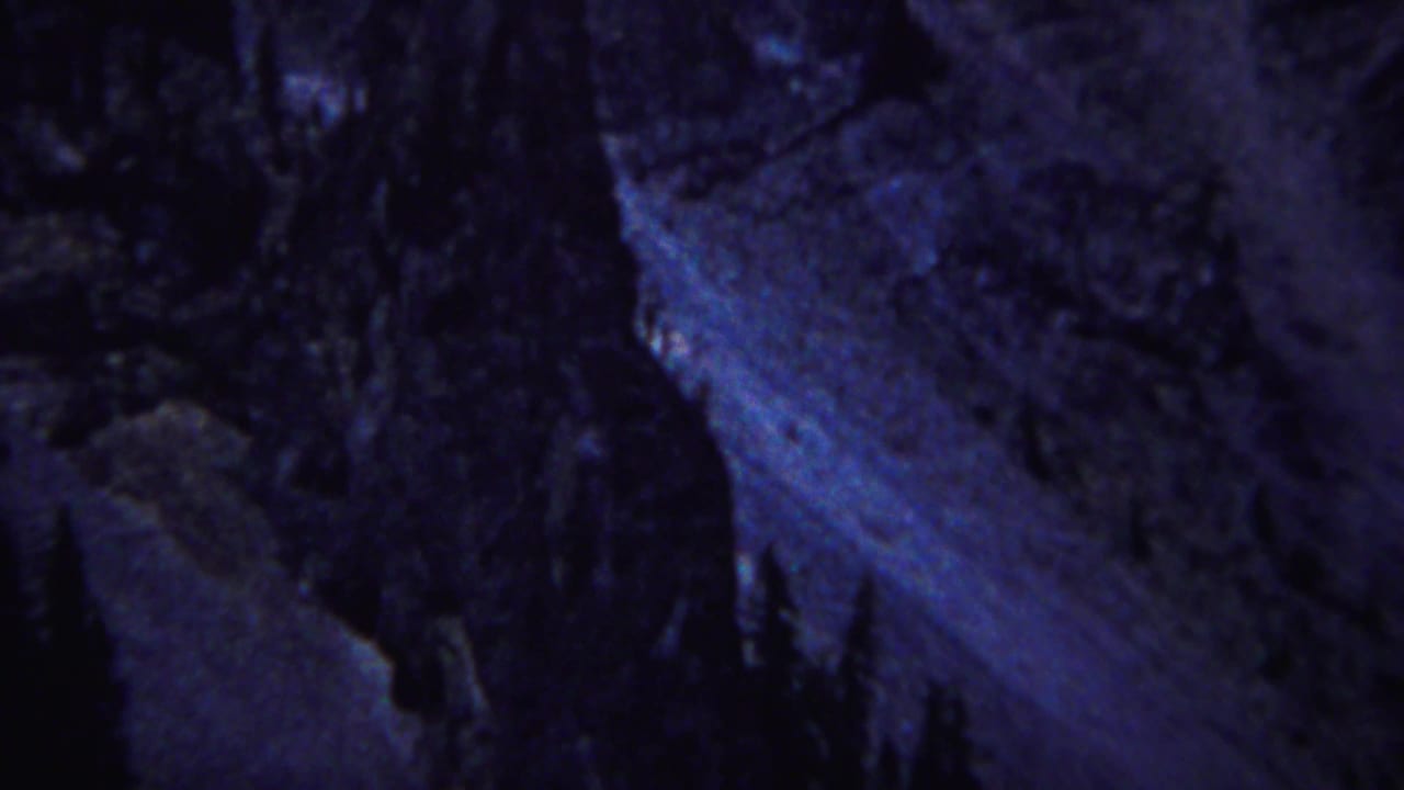 Shadowed mountain wall with dark trees against blue-tinted rock.
