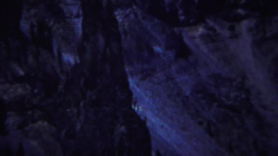 Low-light Yellowstone frame with cave-like rock texture, heavy shadow, and blue highlights from 8mm film.