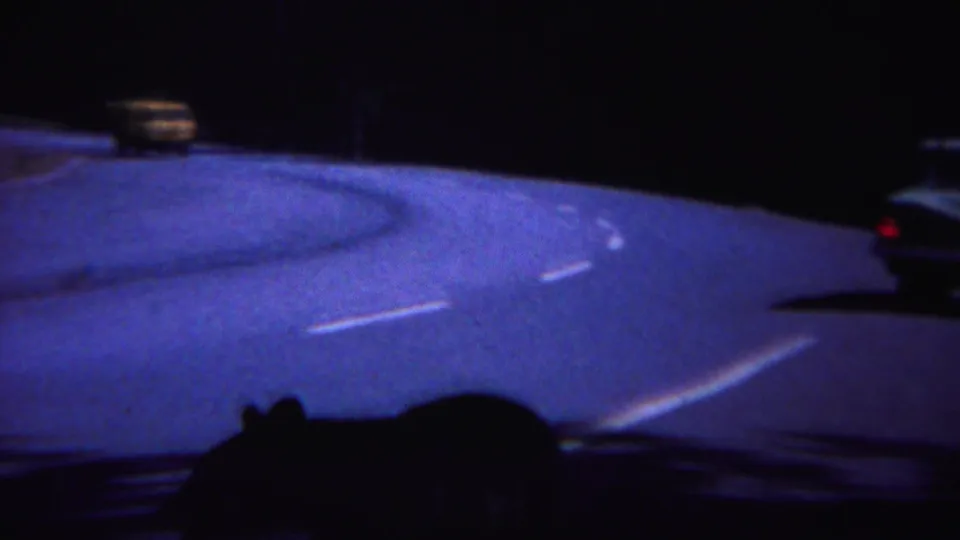 In 1967 Yellowstone home-movie footage, a dark bear silhouette moves near a winding road lit by passing cars at night.