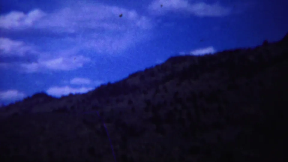 Daytime 1967 Yellowstone landscape footage shows a blue-toned sky over a dark rugged hillside.