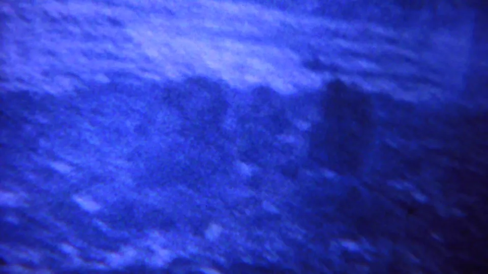 1967 8mm Yellowstone frame showing close, motion-blurred terrain and vegetation with bright blue exposure and heavy grain.