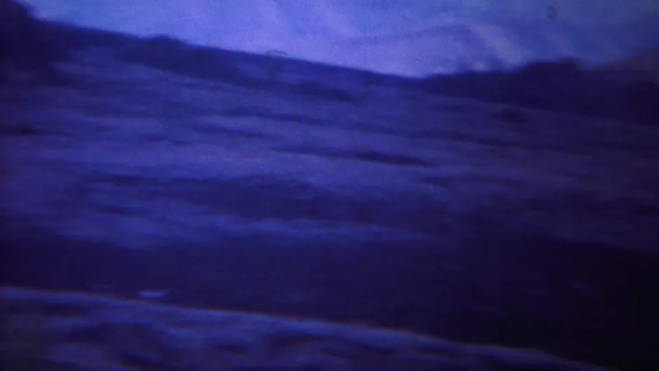 1967 Yellowstone 8mm frame with a distant hilly ridgeline, dark foreground terrain, and blue-purple sky seen from a moving car.