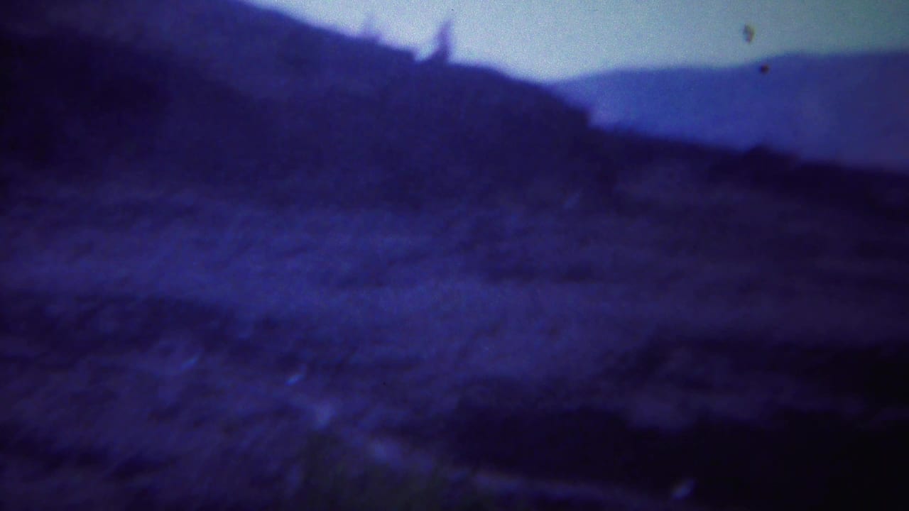 Dark blue mountain ridge and sloping barren terrain under a pale sky.