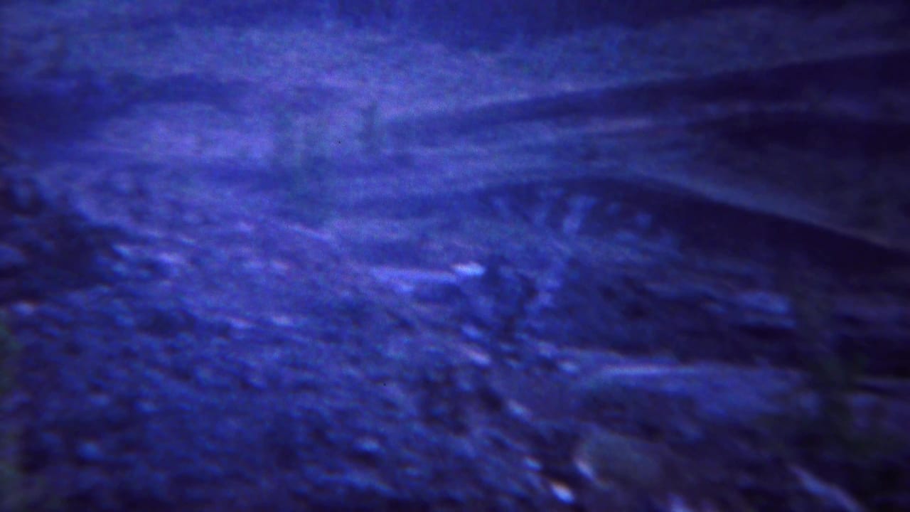 Soft blue-tinted view of rocky hillside terrain and a dark slope beyond.