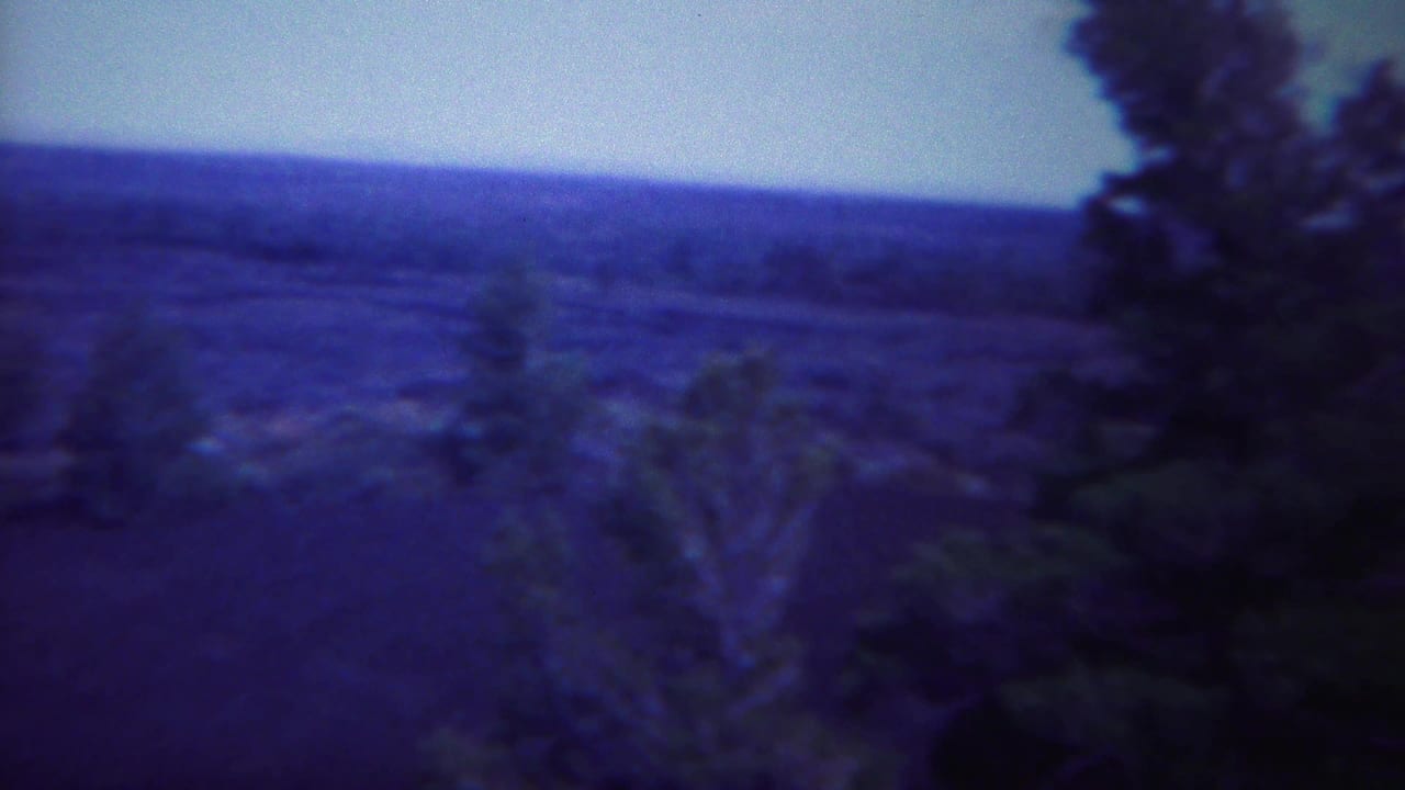 Soft blue-purple view across rocky hills with sparse trees and distant ridges.