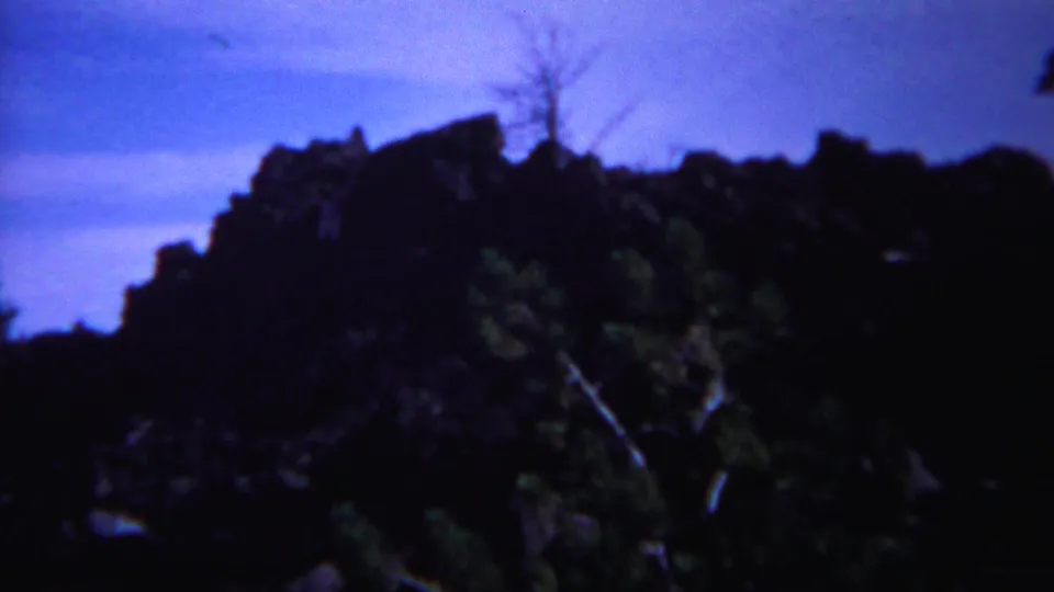 A brief Yellowstone landscape view shows dark rock formations, trees, and blue sky in 1967 home-movie color.