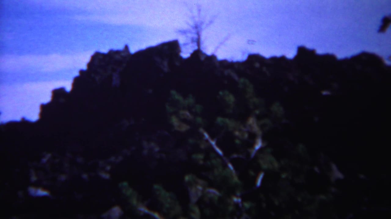 1967 Yellowstone 8mm frame showing a dark rocky outcrop with sparse foliage against a blue sky.