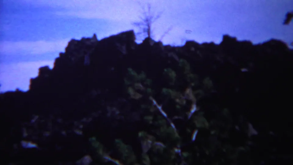 1967 Yellowstone 8mm frame showing a dark rocky outcrop with sparse foliage against a blue sky.