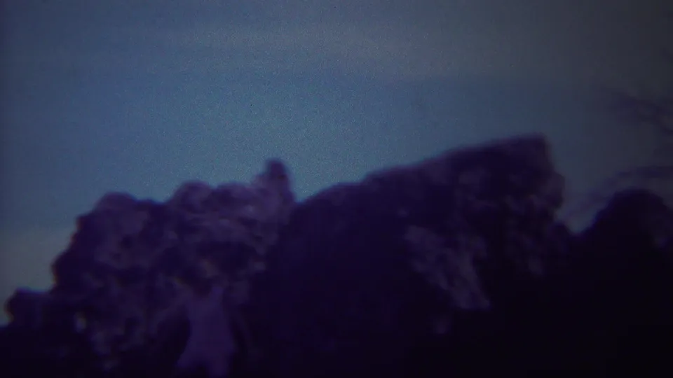 1967 Yellowstone home-movie frame with shadowed rock shapes below a muted blue sky.