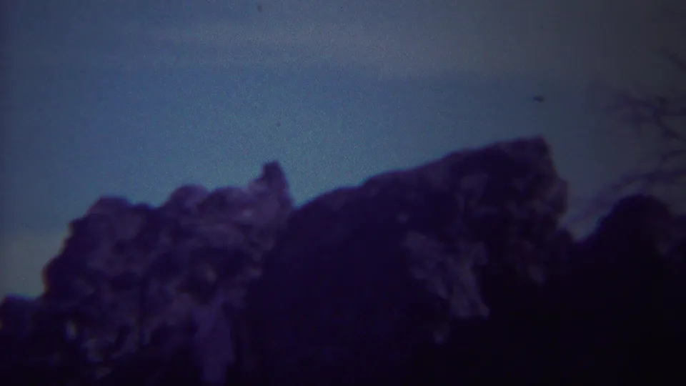 Vintage 8mm Yellowstone view of a rocky outcrop in silhouette with faint tree branches nearby.