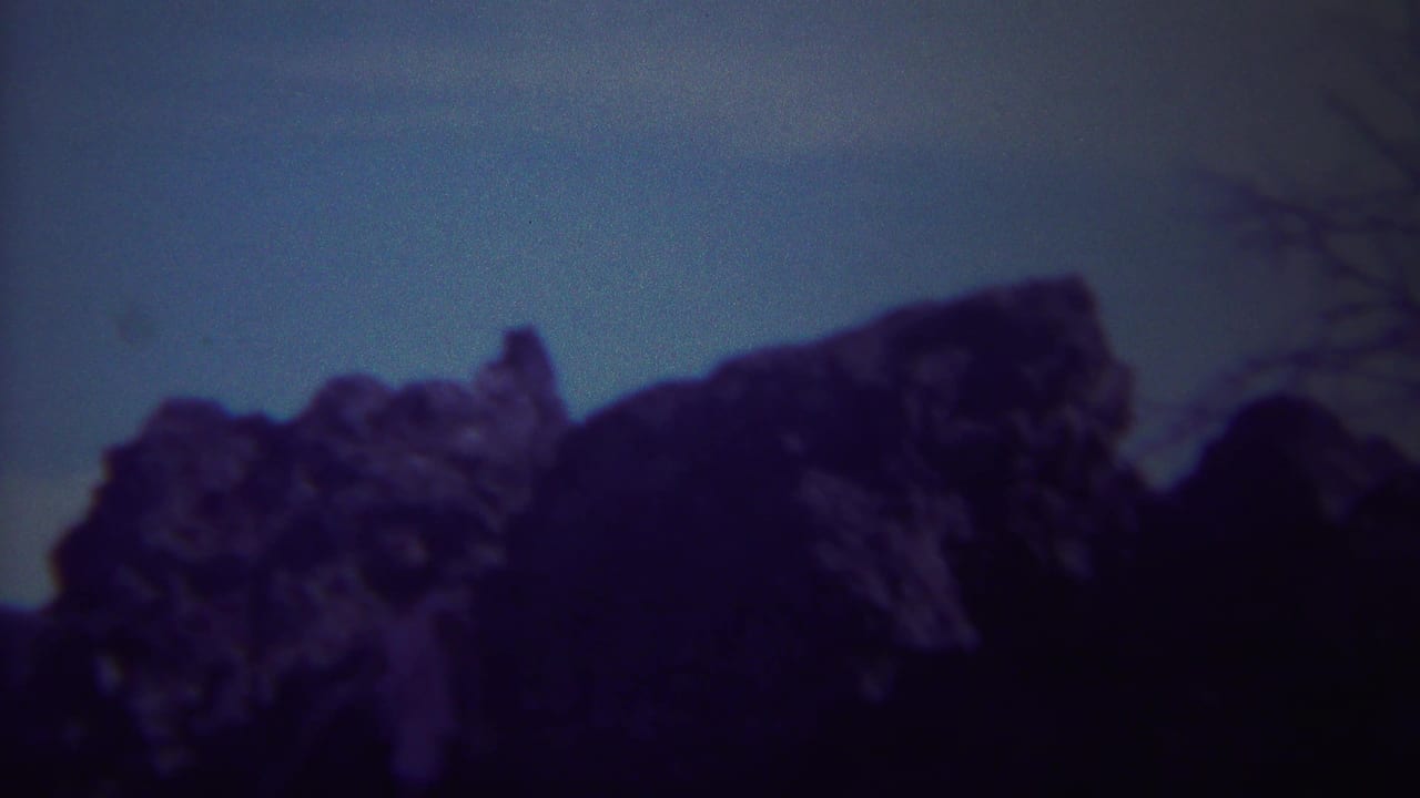 1967 Yellowstone home-movie frame showing shadowed jagged rock formations with a cool blue-purple film cast.