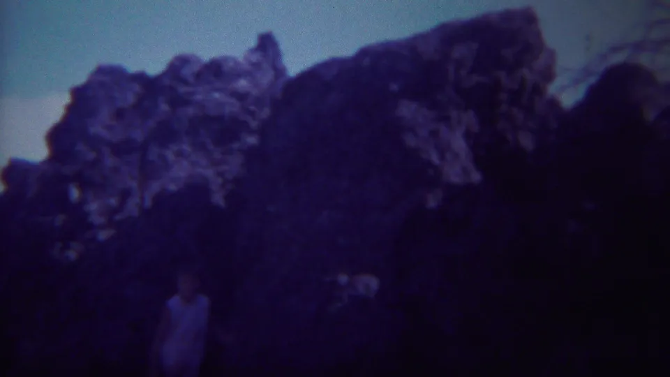 1967 Yellowstone home-movie view of a large shadowed rock formation beneath a pale sky, with soft 8mm grain.