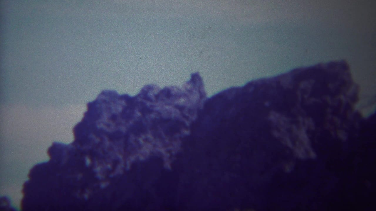 Dark jagged rock formation against a pale sky with blue-purple film cast.