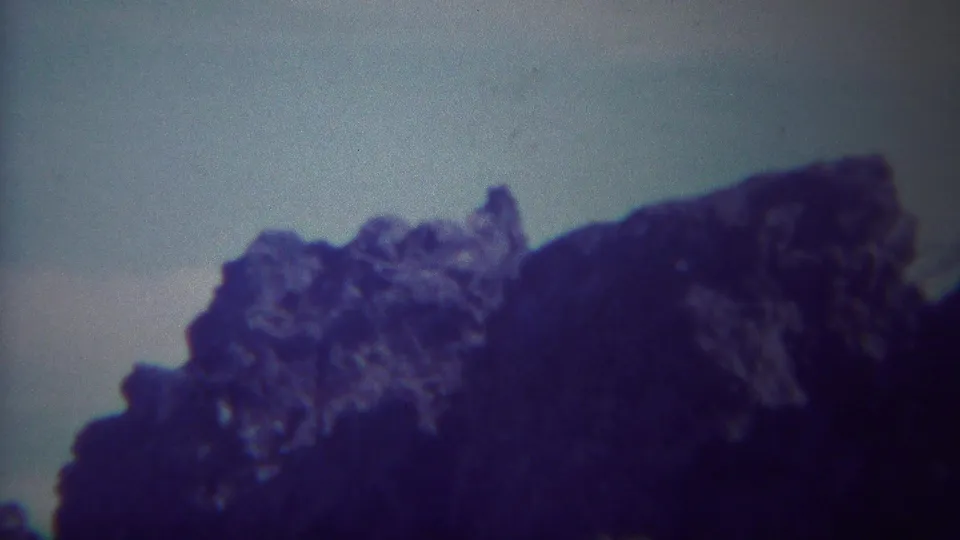 1967 Yellowstone-area 8mm frame showing a dark, jagged rock formation under a pale sky with strong blue-purple color shift.