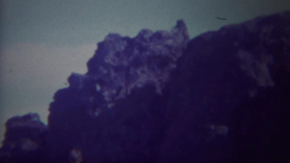 A handheld 8mm view of a large dark rock mass in the Yellowstone-area landscape, with faded color and soft exposure.