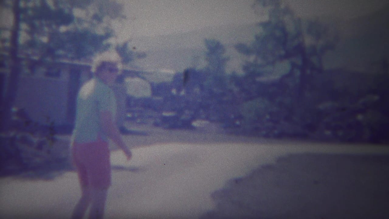Adult woman walking on a paved path near trees and low buildings.