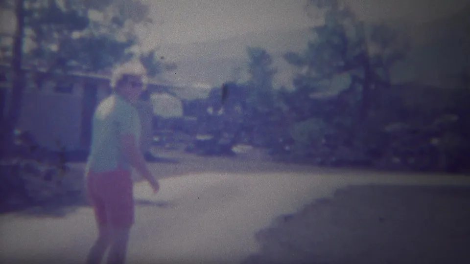 Adult woman in red shorts walking along a paved path in Yellowstone, with trees and low buildings in the background.