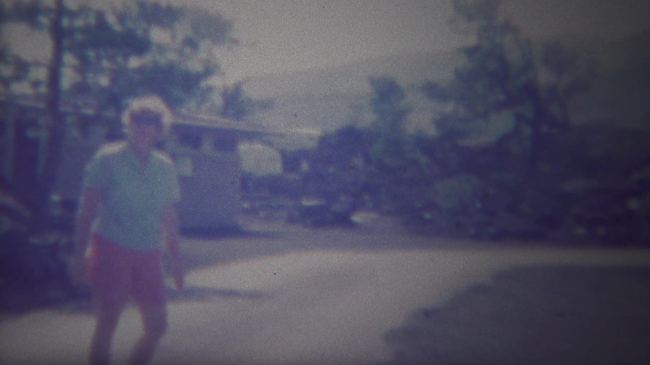 Adult woman standing or walking on a sunlit path with trees behind her.
