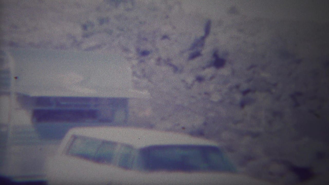 1967 Yellowstone home-movie frame showing a light blue and white camper trailer with a white station wagon parked beside it.