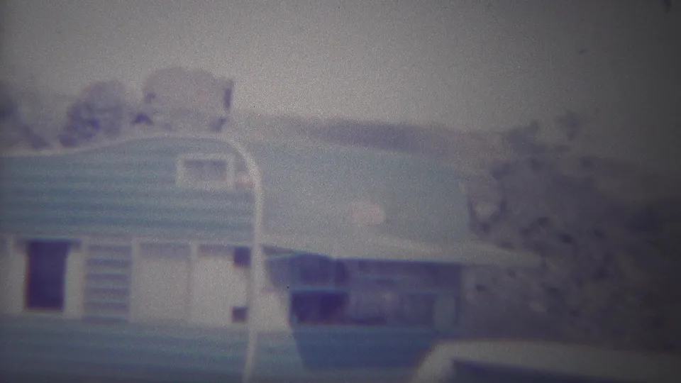 1967 Yellowstone frame with the camper trailer centered, showing its rounded roof, blue stripe, side door area, and trees on a rocky hillside.