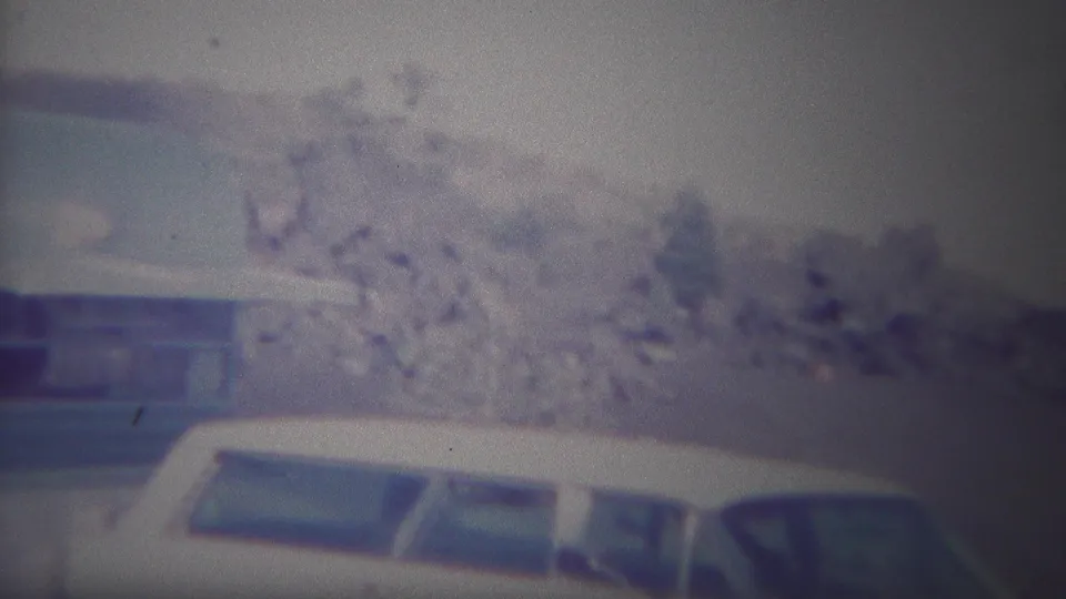 1967 Yellowstone frame showing a white vehicle across the foreground and the blue-and-white camping trailer set behind it near trees and open hillside.
