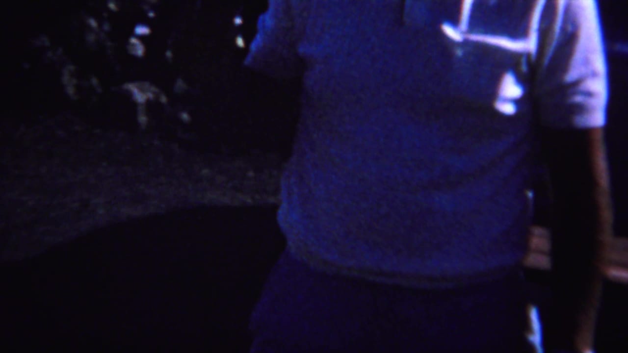 1967 Yellowstone-area 8mm frame showing an adult in a light shirt standing outdoors at night near partially visible people.