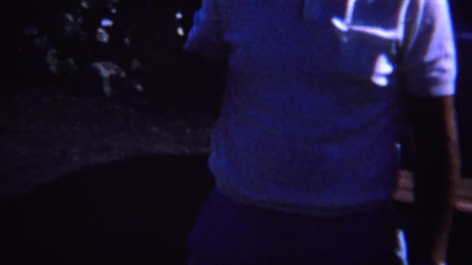 1967 Yellowstone-area 8mm frame showing an adult in a light shirt standing outdoors at night near partially visible people.