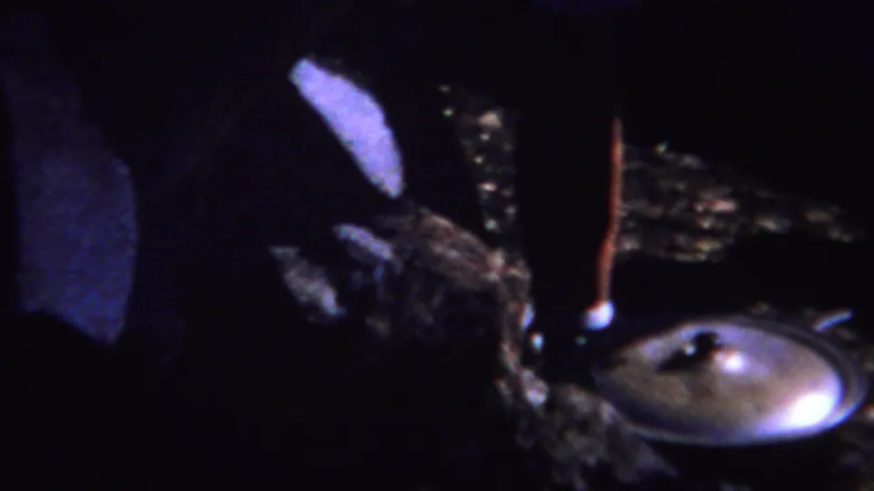 1967 Yellowstone-area 8mm frame showing an adult bending beside a metal fire pit or lid in a dim outdoor setting.