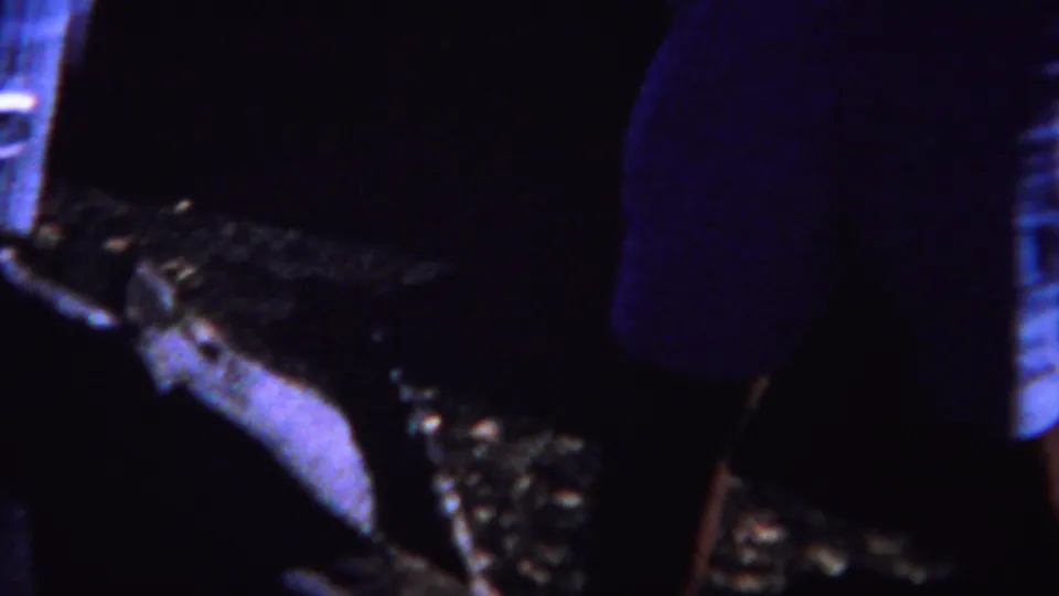 1967 Yellowstone-area home-movie frame with an adult standing near a low fire pit area under blue-purple nighttime lighting.